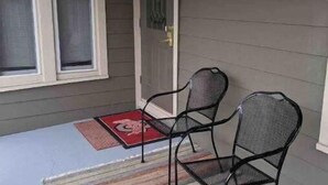 Une véranda avec deux chaises en métal et un tapis à rayures.