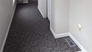 En hall med ett heltäckningsmatta på golvet, en dörr, en liten växt och en dekorativ detalj som hänger på väggen.