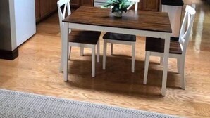 Ett kök med träskåp, ett vitt kylskåp, en mikrovågsugn, en ugn och ett matbord med fyra stolar.