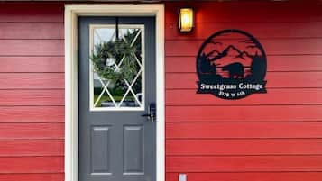 A red building with a gray door, a window with a plant, and a logo for Sweetgrass Cottage at 3178 W 4th.