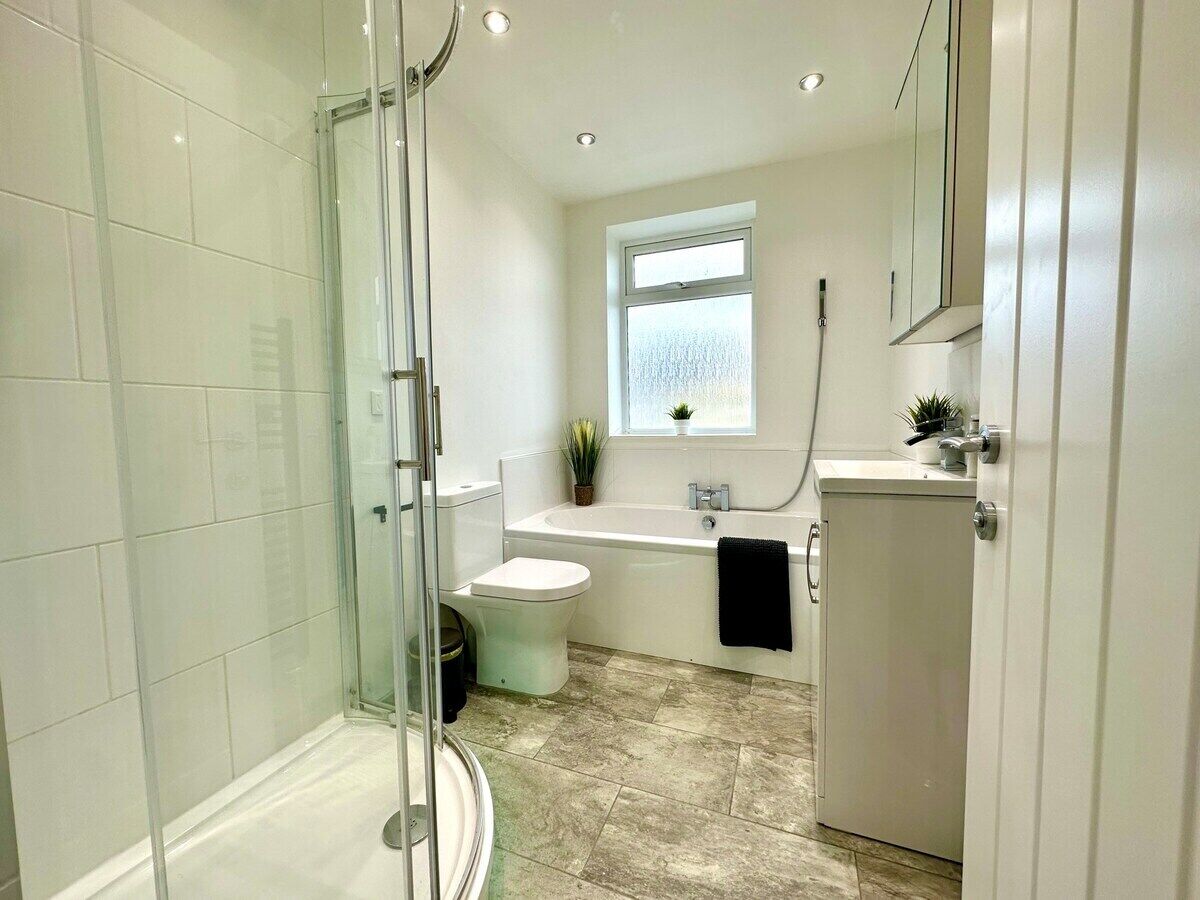 A modern bathroom with a glass shower enclosure, a toilet, a bathtub, and a sink.