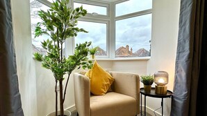 Una habitación de esquina con un sillón beige, una planta en maceta y una mesita con una lámpara.