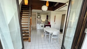 A compact kitchen with a dining area, a staircase, and a sliding glass door leading to a balcony. - Charming cocoon (Cabourg)