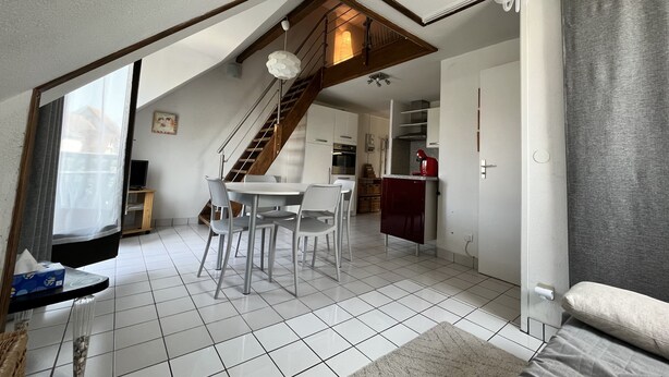A modern kitchen with white cabinets, a red appliance, and a staircase leading to an upper level. - Charming cocoon (Cabourg)