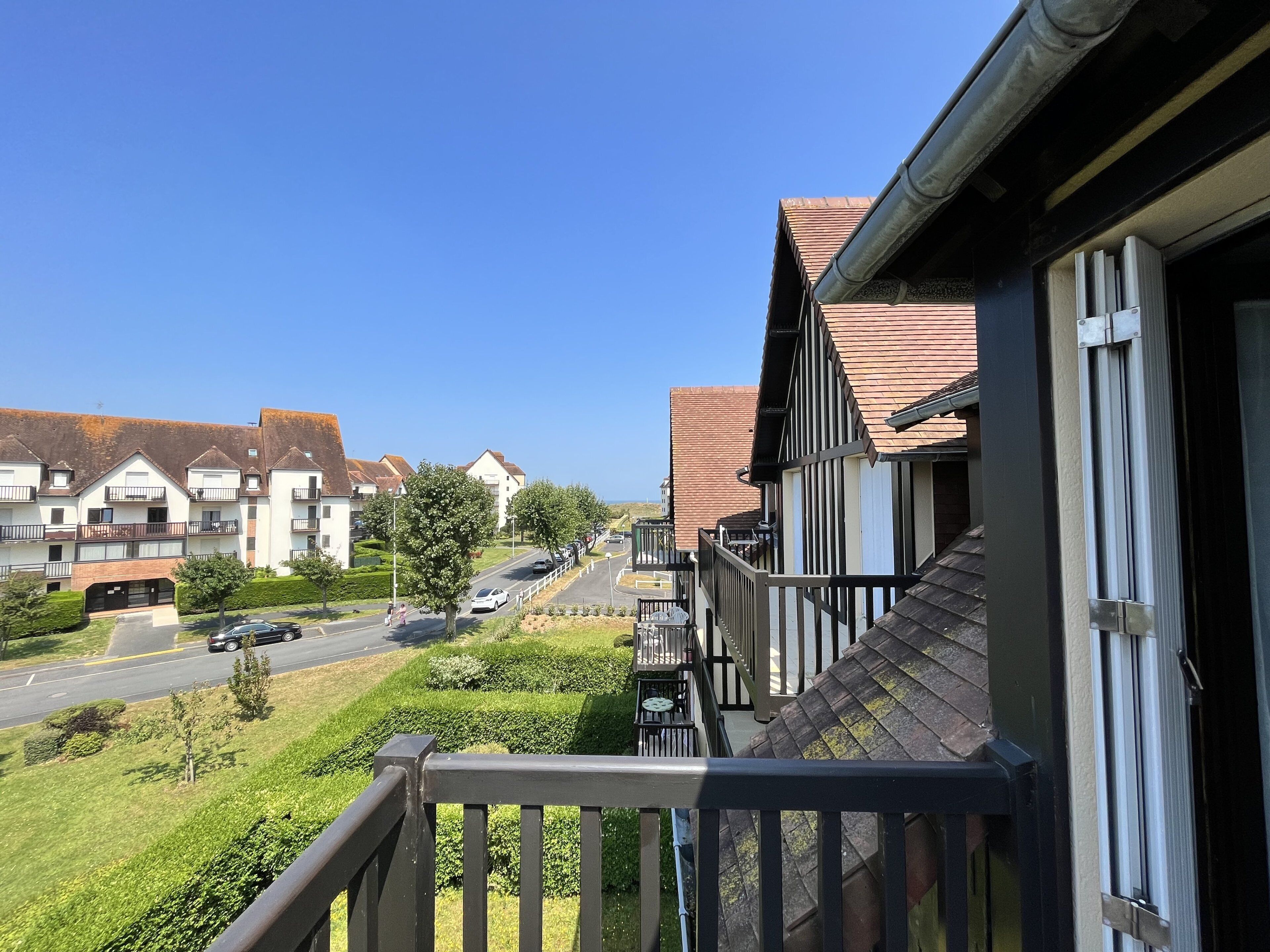 Une rue résidentielle bordée de maisons, un ciel dégagé et une route où circulent des voitures.
