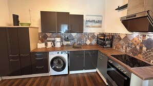A compact kitchen with a washing machine, a coffee maker, and a microwave. - 50sqm apartment with two terraces, barbecue area and large outdoor area (Putbus)