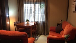 Een woonkamer met een eethoek, een bank, een klein tafeltje met een vaas en een airconditioner aan de muur.