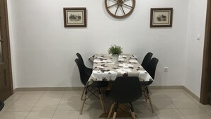 Een eethoek met een tafel voor vier personen, aan weerszijden omlijst door twee foto's, een decoratief wiel en een potplant.