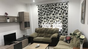 Een moderne woonkamer met een bank, een salontafel, een televisie en een decoratieve vaas.