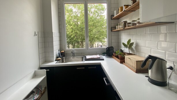 A modern kitchen with white tiles, a window with a view of trees, a sink, and a kettle. - Cosy, calme et lumineux à Paris Bastille - 2mn du métro (Paris)