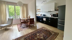 A modern kitchen with a washing machine, a dining area with a table and chairs, and a view of greenery outside. - Cosy, calme et lumineux à Paris Bastille - 2mn du métro (Paris)