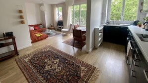 A spacious living area with a large rug, a sofa, a dining table, and a kitchen with a window. - Cosy, calme et lumineux à Paris Bastille - 2mn du métro (Paris)