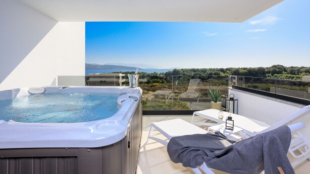 Een balkon met een hottub, een tafel met een glas, en uitzicht op het landschap.