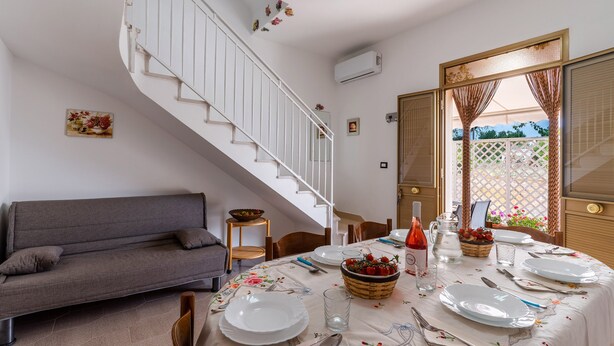 Ein Essbereich mit Tisch für vier Personen, einer Couch, einer Treppe und Blick durch eine Tür.