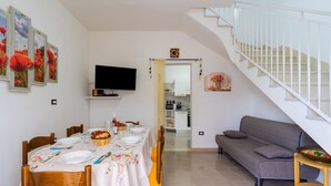 Ein Essbereich mit Tisch für vier Personen, einer Couch, einem Fernseher und einer Treppe.