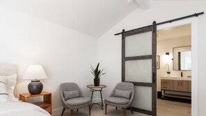 A bedroom with a bed, two armchairs, a small table with a lamp, and a sliding door leading to a bathroom. - Studio Bella - Solvang, CA (Solvang)