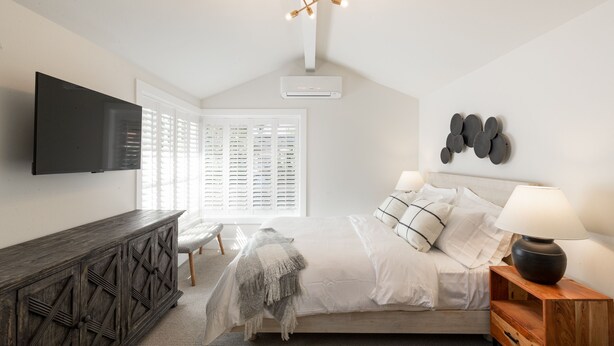 A bedroom with a bed, bedside table, lamp, TV, and a window with blinds. - Studio Bella - Solvang, CA (Solvang)