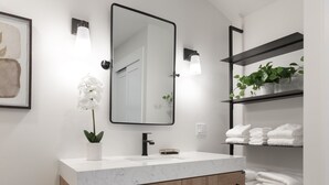 A modern bathroom with a marble sink, wooden cabinets, a large mirror, and a shelf with folded towels. - Studio Bella - Solvang, CA (Solvang)
