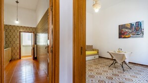 A room with patterned flooring, a bed, a table with a tablecloth, and a painting on the wall.