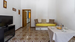 A small, clean room with a bed, a TV, a table with breakfast, and patterned flooring.