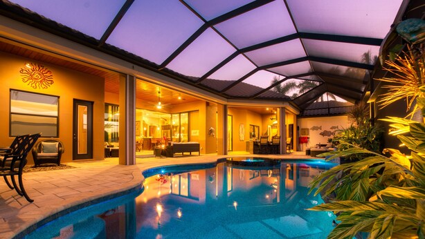 A swimming pool with a glass ceiling, indoor seating area, and a view of the sunset. - Intervillas Florida - Bella Villa 141 (Cape Coral)