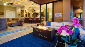 A modern living room with a fireplace, sofas, and a dining area visible through glass doors. - Intervillas Florida - Bella Villa 141 (Cape Coral)