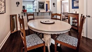A dining area with a round table, six wooden chairs with patterned cushions, and a white wall with a blackboard and a framed picture.