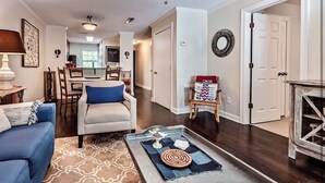 A living room with a blue sofa, a coffee table with decorative items, a patterned rug, and a dining area in the background.
