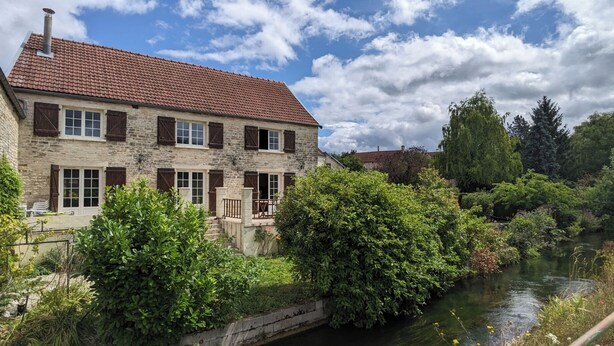 A stone house with a tiled roof, a small bridge, and a river.