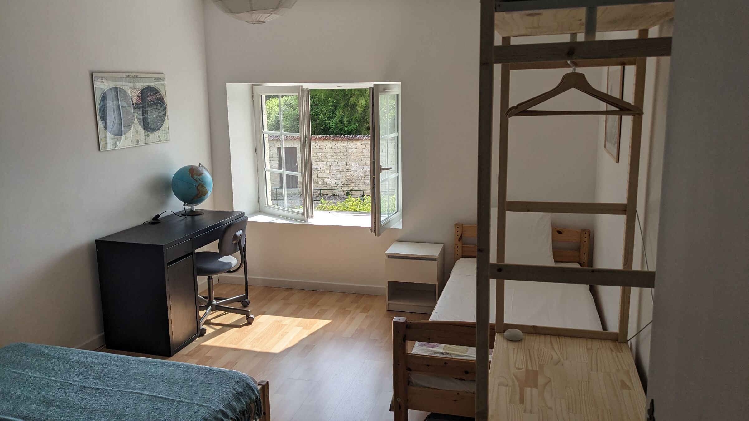 A room with a desk, chair, bunk bed, and a window with a view of greenery.