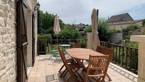 An outdoor patio with a wooden table and chairs, a green umbrella, and a stone wall.