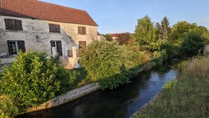 A stone building with a red-tiled roof, adjacent to a narrow water channel.