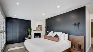 A modern bedroom with a large bed, dark walls, and a fireplace. - Off-Broadway • Boho Modern 3BR • King Suite • Huge Yard + Treehouse • Near River & Downtown (Boise)