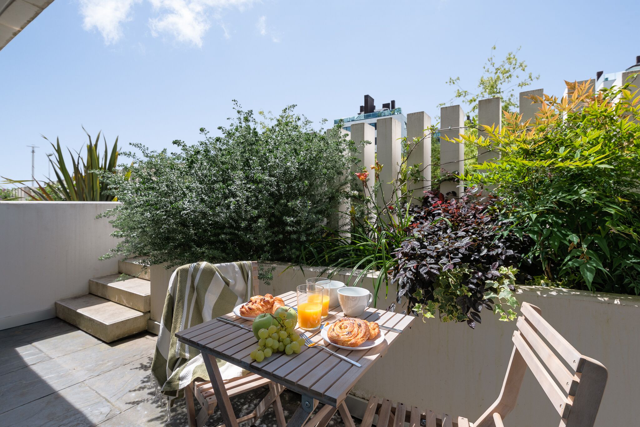 Un patio con una mesa dispuesta para el desayuno, que incluye cruasanes, uvas y jugo de naranja.
