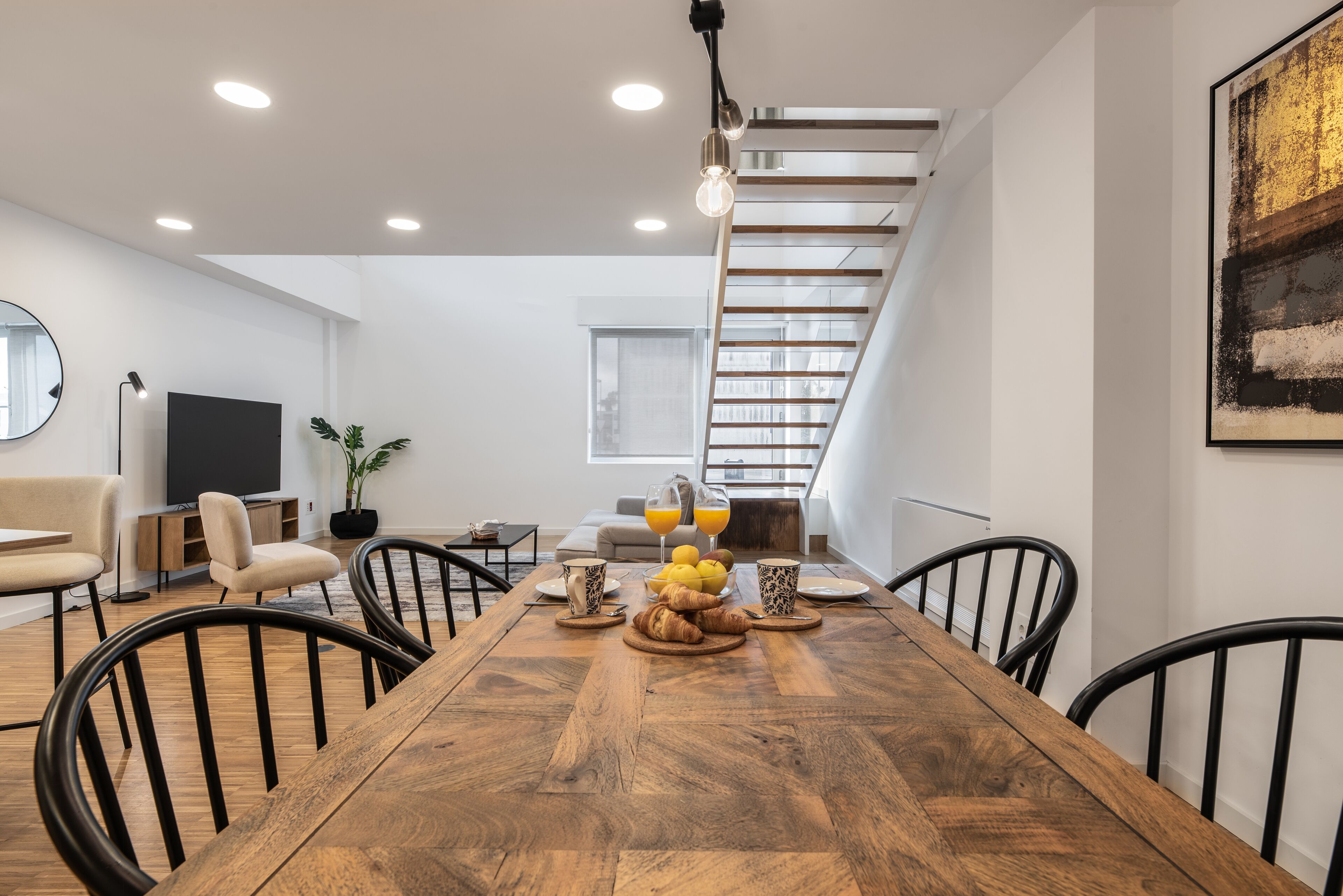 Een moderne eetruimte met een houten tafel, zwarte stoelen en een trap op de achtergrond.