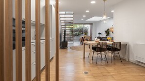 A modern kitchen with wooden cabinets, a dining area with a wooden table and chairs, and a staircase leading to an upper level.