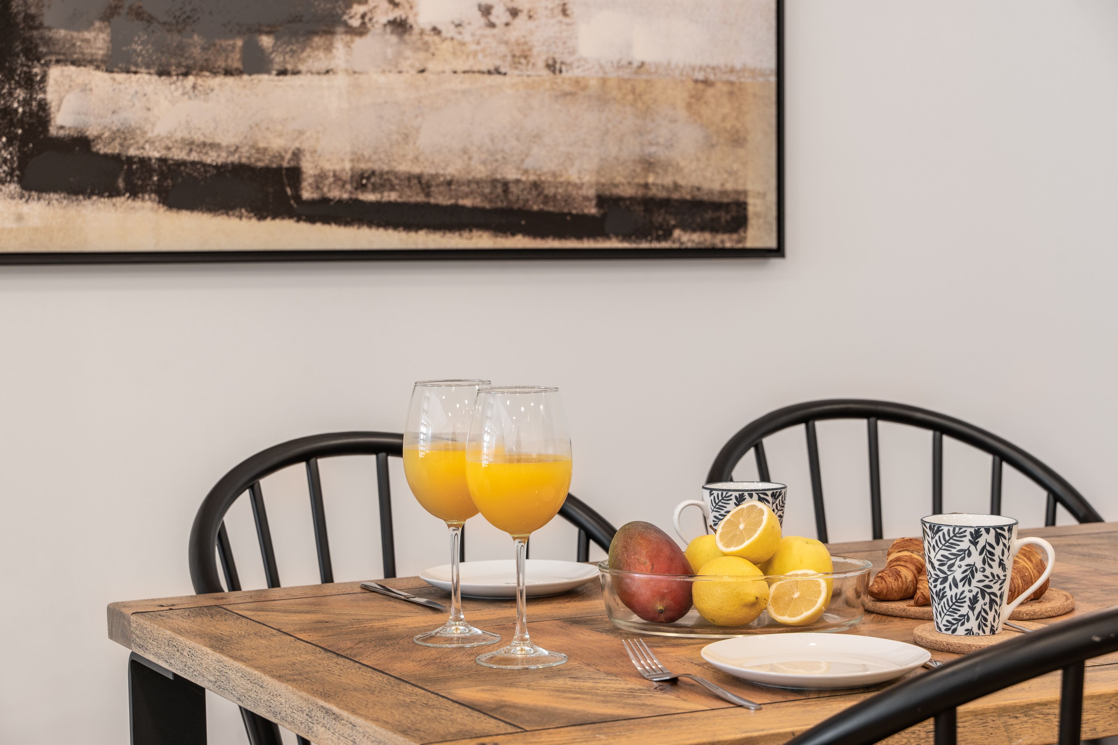 Ein Holztisch mit zwei Orangensaftgläsern, einer Obstschale, einem Teller und einer Tasse.