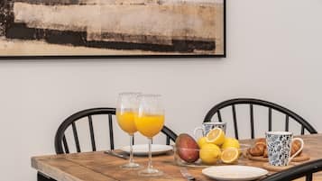 Ein Holztisch mit zwei Orangensaftgläsern, einer Obstschale, einem Teller und einer Tasse.