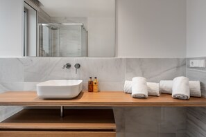 A modern bathroom with a large white sink, a glass shower enclosure, and neatly folded white towels on a wooden vanity.