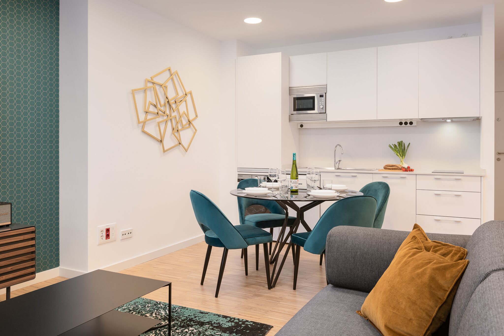 A modern kitchen with white cabinets, a microwave, and a dining area with teal chairs and a glass table.
