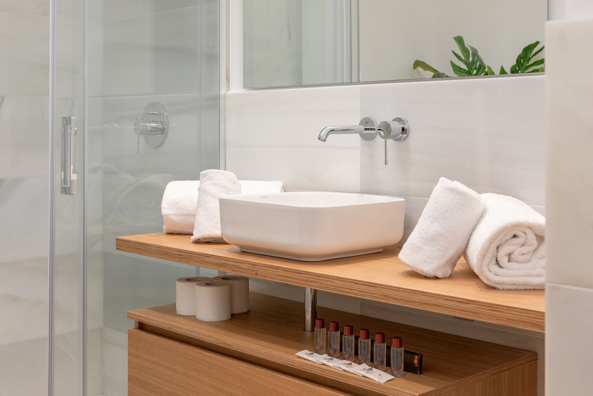 Een moderne badkamer met een glazen douchecabine, een witte wastafel met houten aanrechtblad en netjes opgevouwen handdoeken.