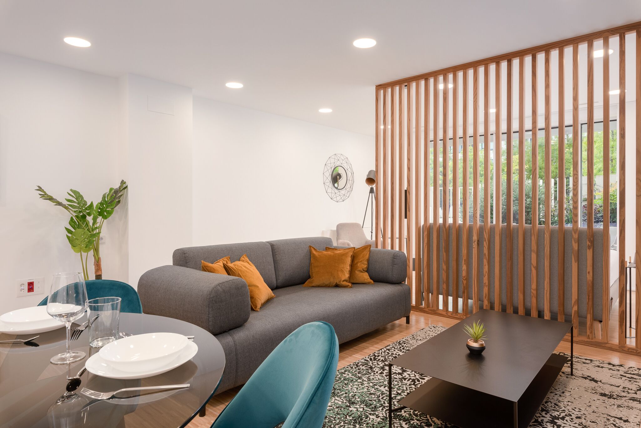 A modern living room with a grey sofa, a dining table set with plates and glasses, a blue chair, and a small potted plant on a black coffee table.