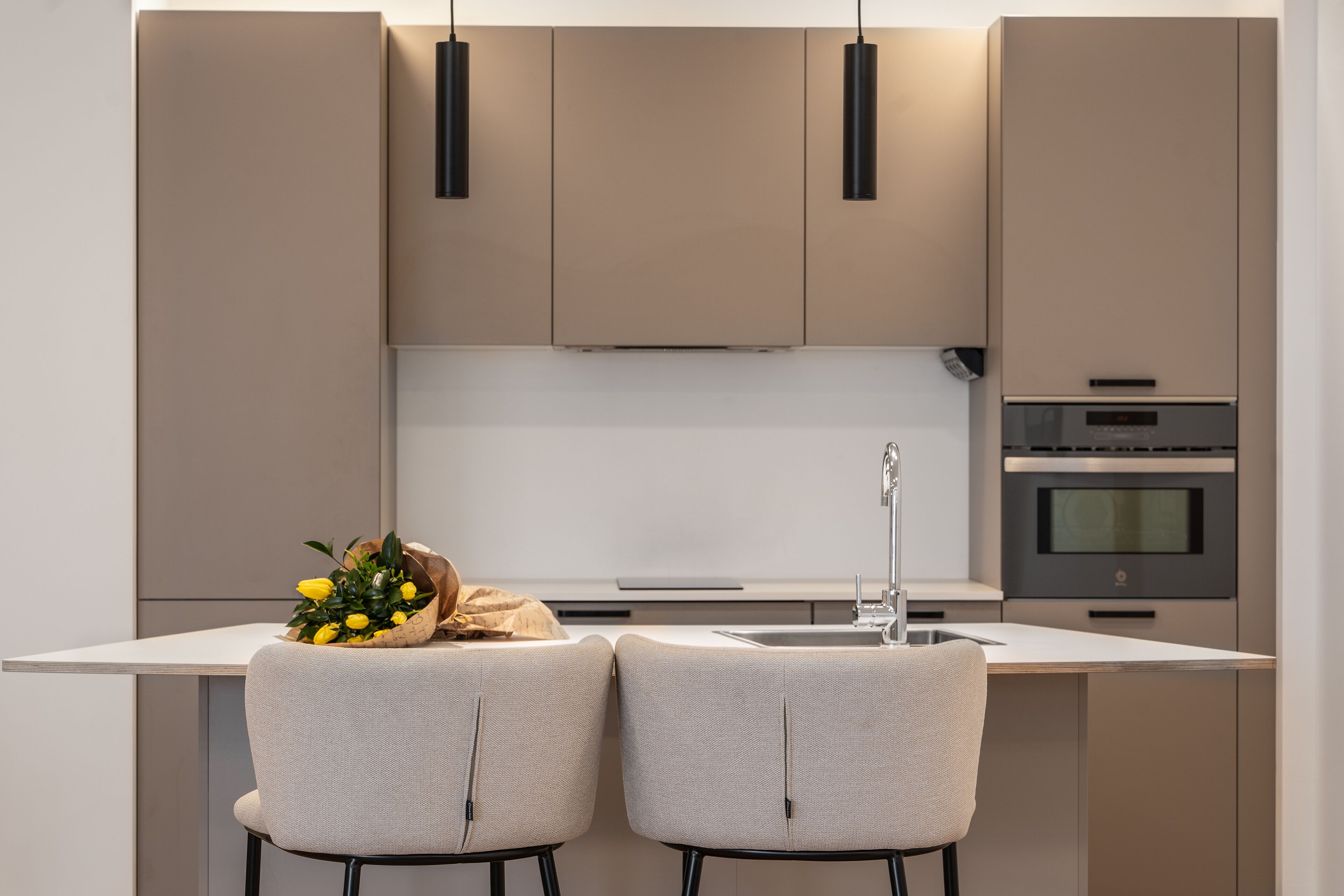 Une cuisine moderne avec deux chaises, un petit îlot central et un four encastré.