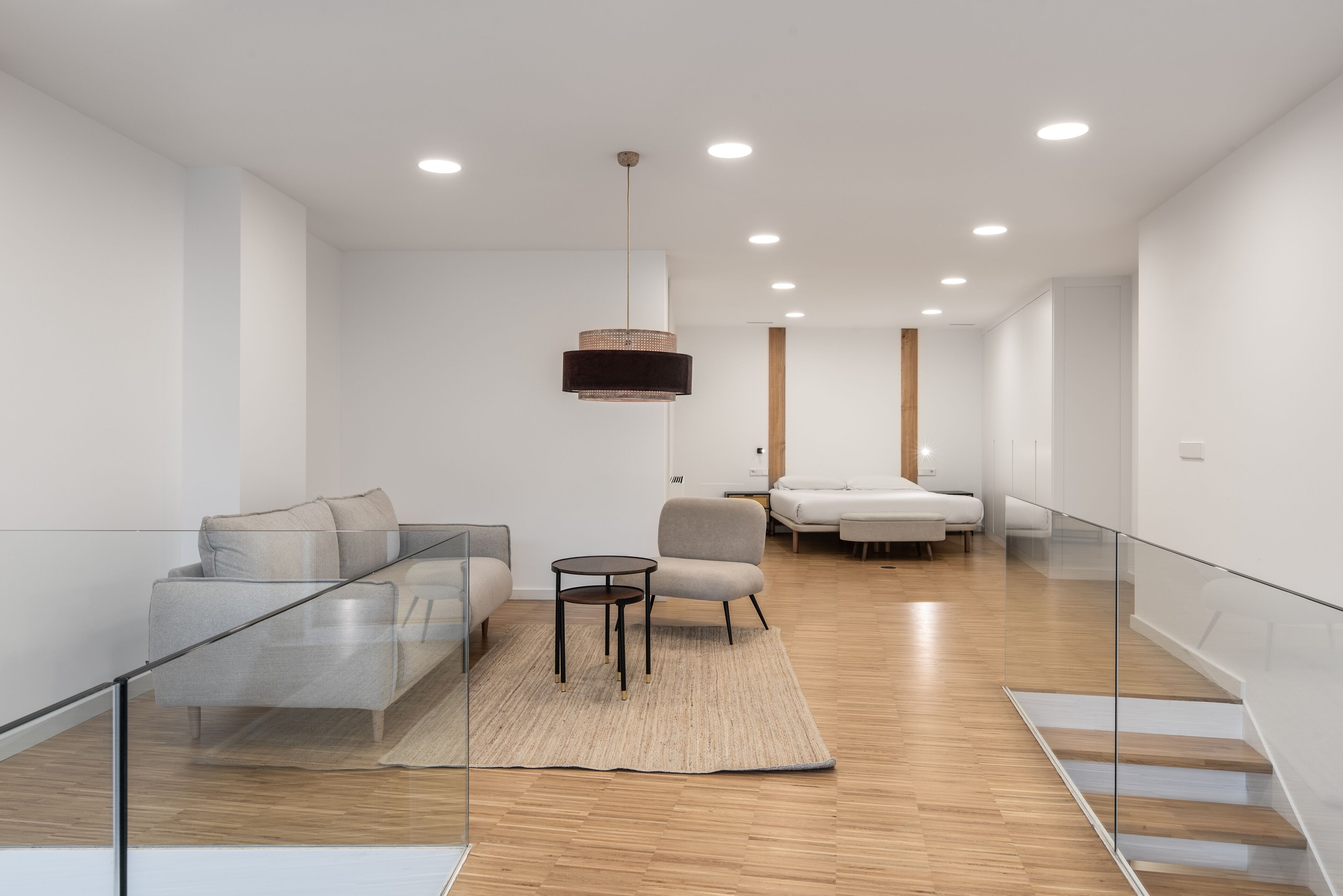 Una sala de estar moderna con un separador de vidrio, un sofá, una silla, una mesita y una lámpara colgante.