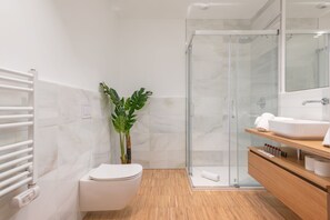 A modern bathroom with a glass shower enclosure, a white toilet, a wooden vanity, and a potted plant. - I Loft Santiago by Upper Luxury Housing (Santiago de Compostela)