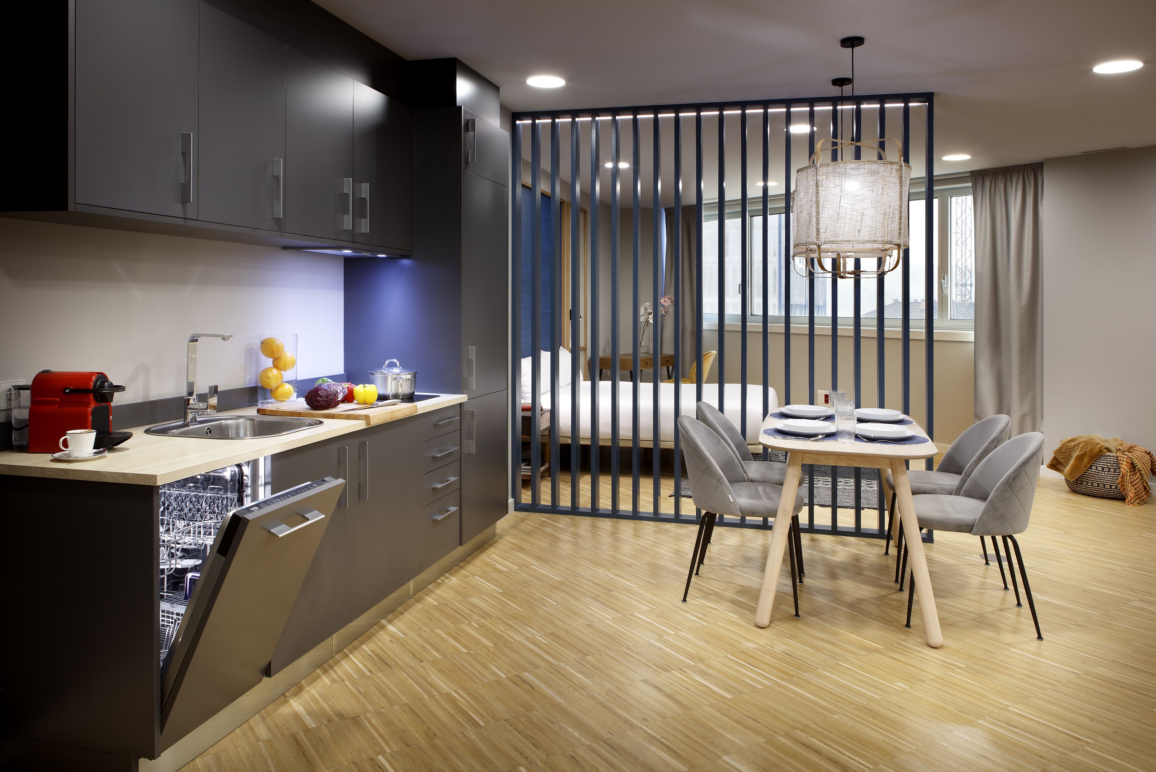 A modern kitchen with a dishwasher, a coffee machine, and a dining area with a table and chairs.