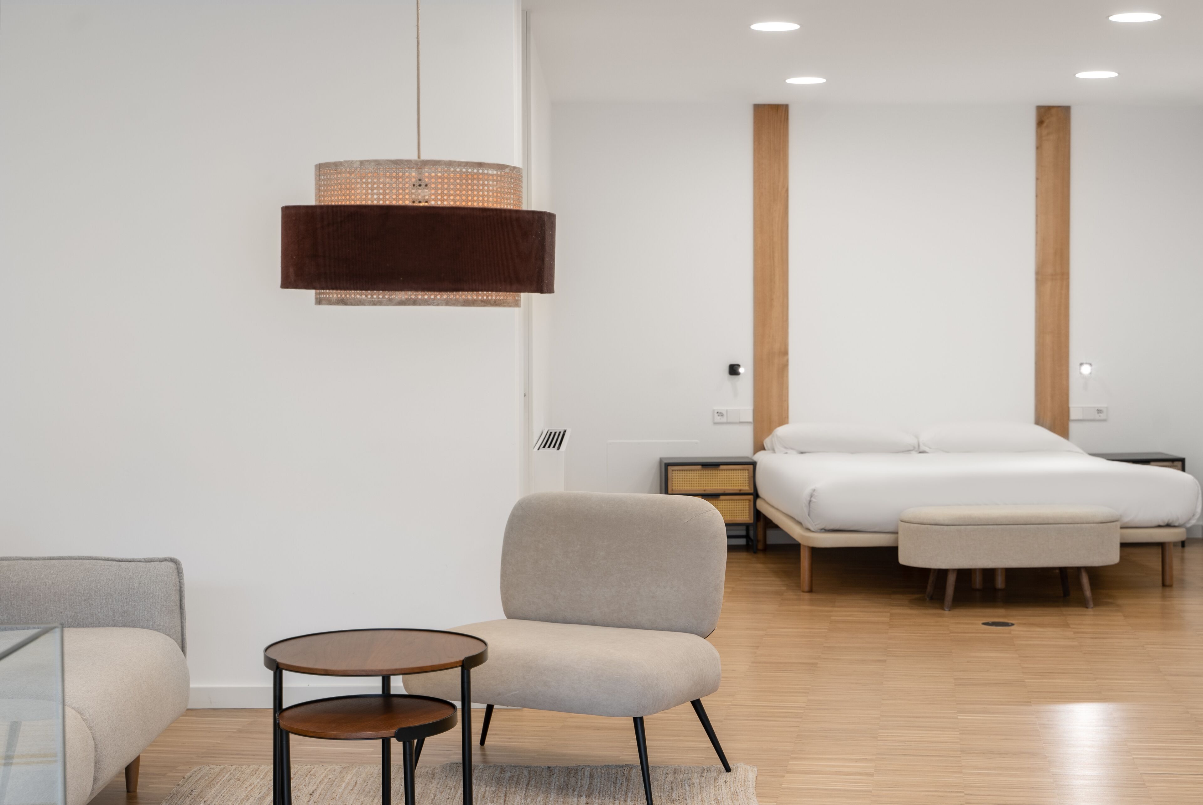 A modern hotel room with a bed, a sofa, a small table, and a hanging light fixture.