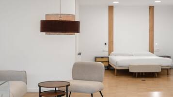 A modern hotel room with a bed, a sofa, a small table, and a hanging light fixture.