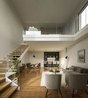 Amplia sala de estar con techo alto, una escalera que sube a un nivel superior y una cocina al fondo.
