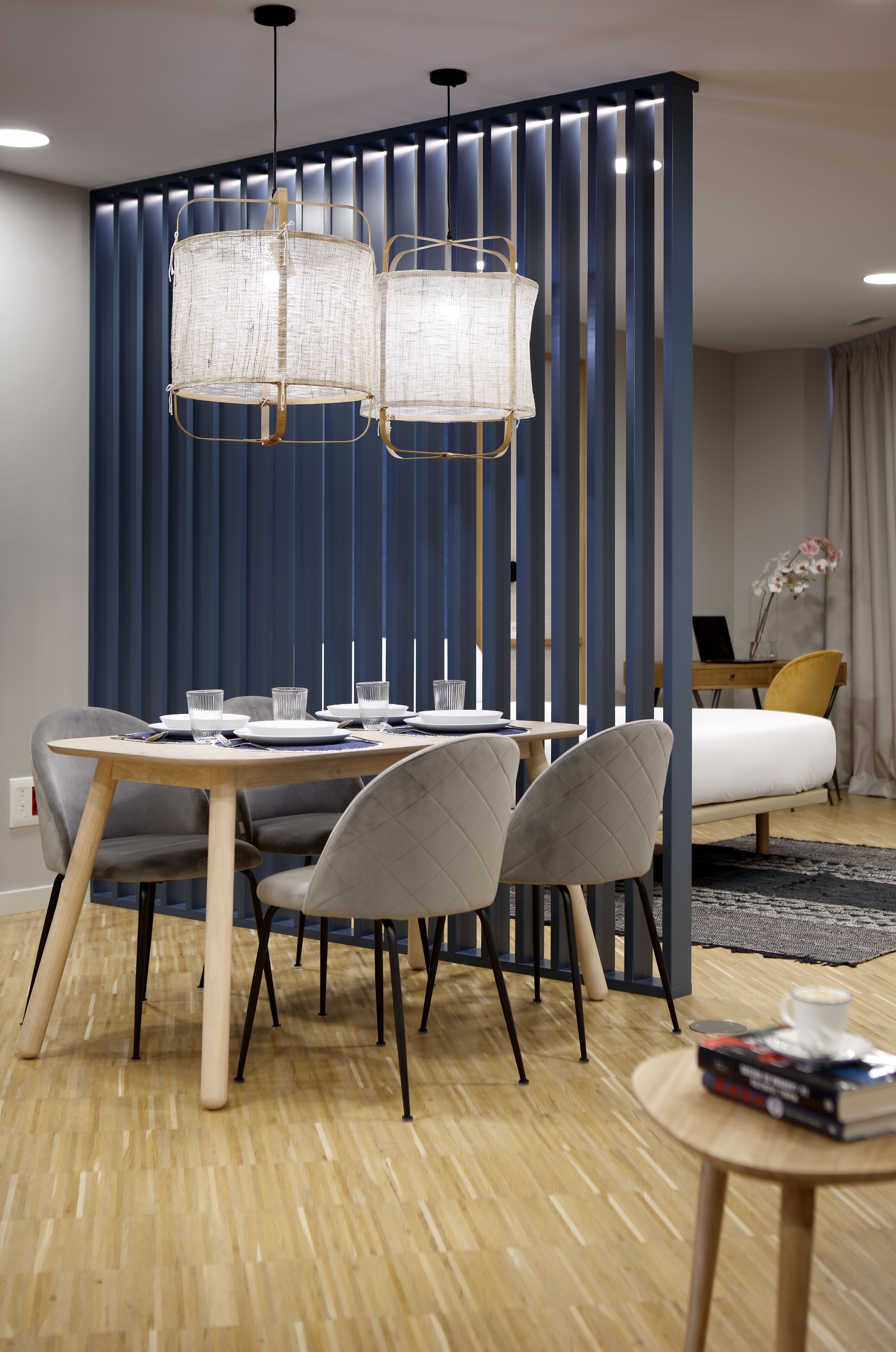 Un espace repas moderne avec une table en bois, des chaises à revêtement gris et un séparateur bleu composé de lattes verticales.